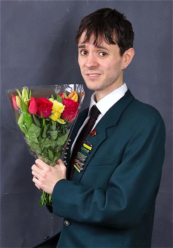 A man poses awkwardly with a bouquet of flowers with an apologetic look on his face