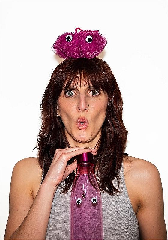 The performer looks at the camera with a shocked expression holding a pink water bottle with googly eyes.