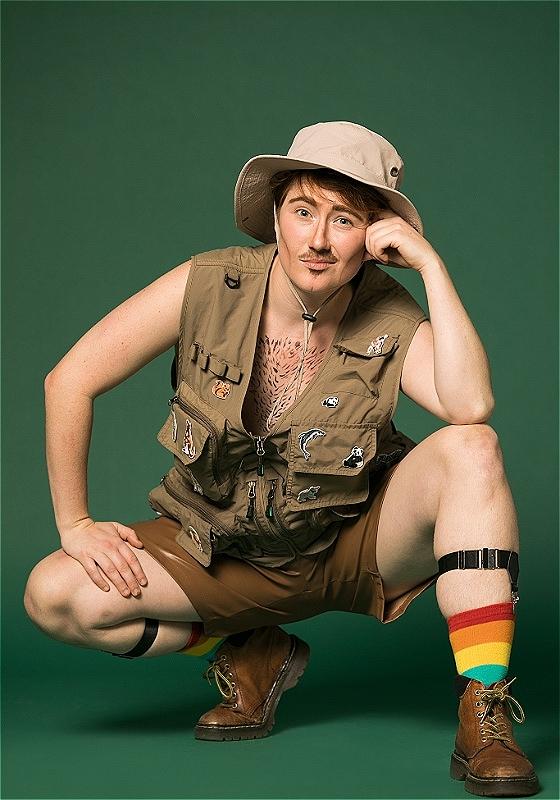 The performer is crouching, dressed like an explorer with a beige hat and rainbow socks.