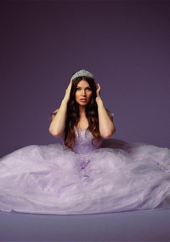 Katie sits on the floor in a poufy purple dress and tiara with a matching background
