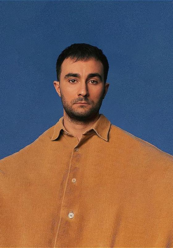 Eddie wears a comically oversized yellow shirt against a blue background.