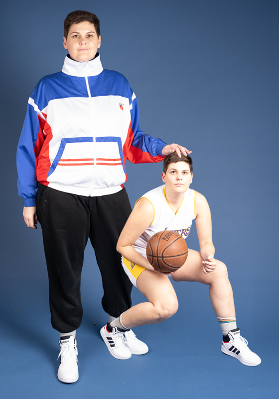 Abby stands is sportwear with their hand touching the head of a miniaturized version of themselves in basketball gear.