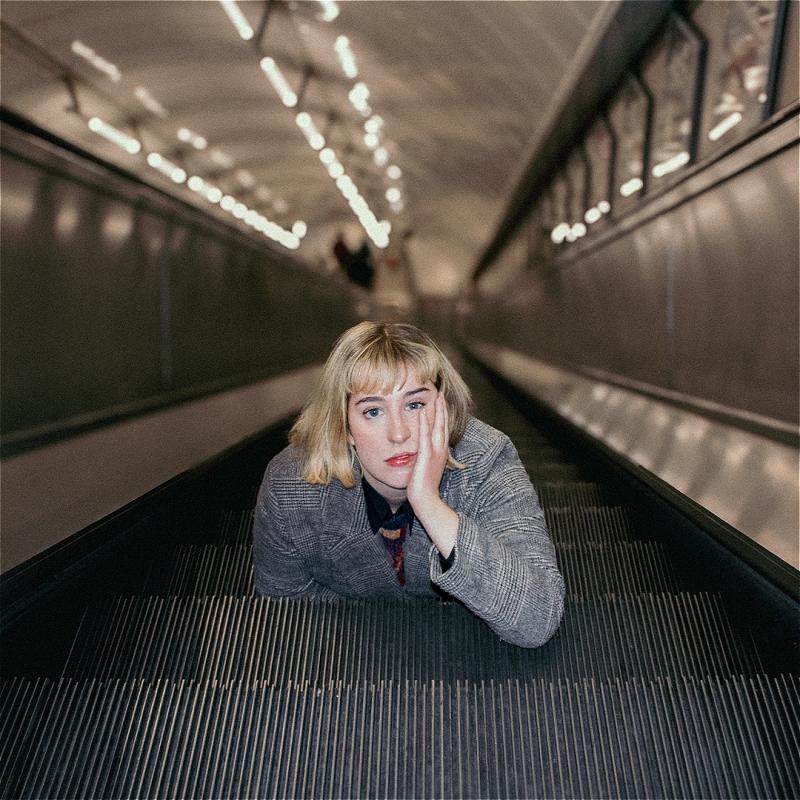 A woman rests her face on her hands as she lies down on an escalator.