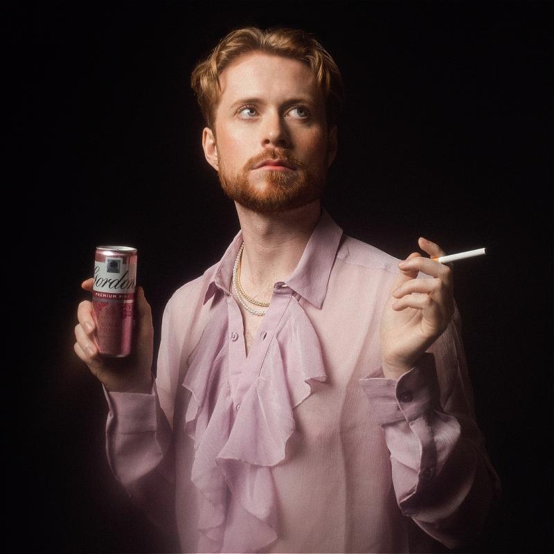 The performer wears a pink blouse and looks upwards. They hold a cigarette in one hand and a can of pink gin in the other. 