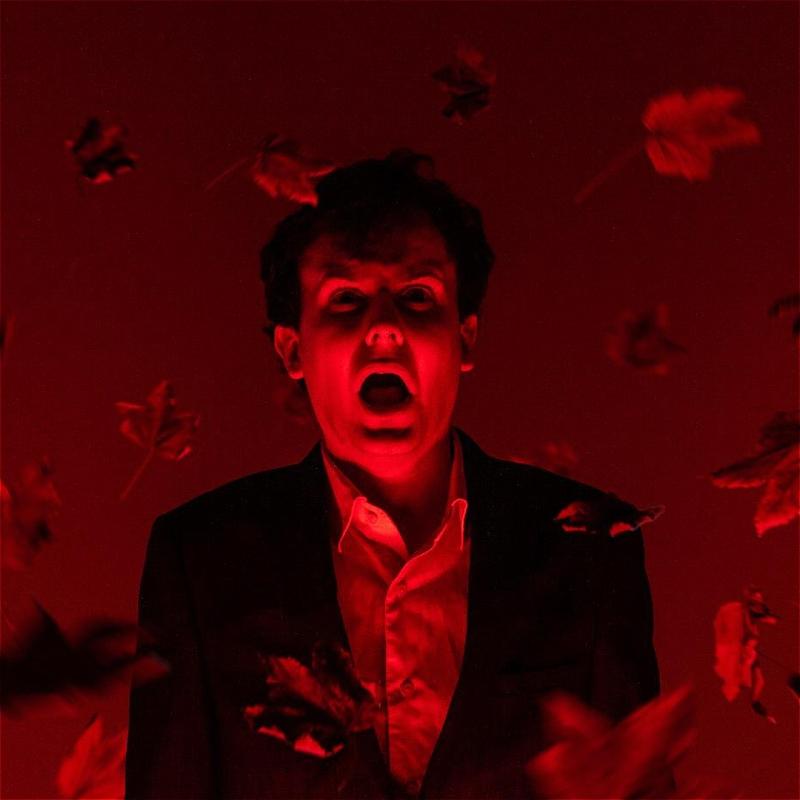 Andrew wears a suit with an expression of horror with harsh red lighting.
