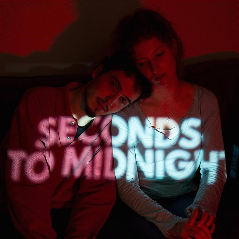 A boy and a girl sit next to each other with the words 'seconds to midnight' projected across their bodies.