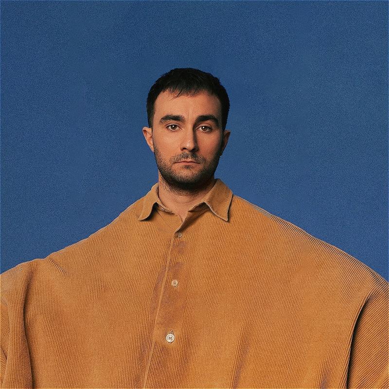 Eddie wears a comically oversized yellow shirt against a blue background.