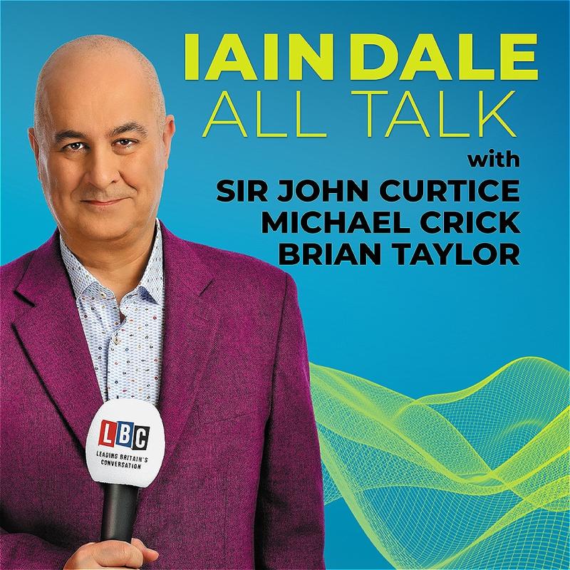 In front of a blue background, Iain Dale wears a purple suit and looks into the camera, holding a mic.