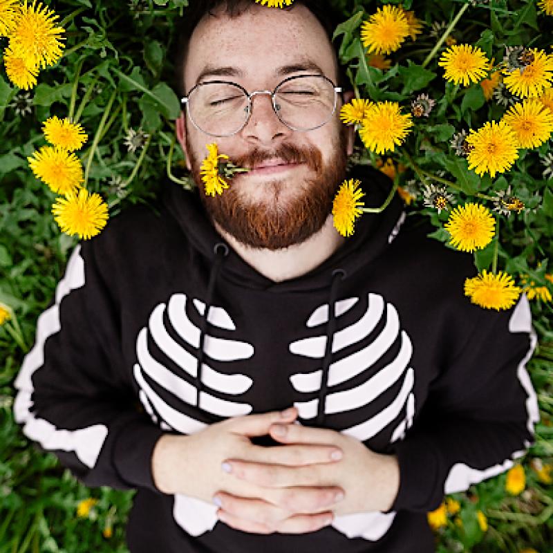 Rich Spalding lying in a field of dandelions wearing a skeleton jumper.